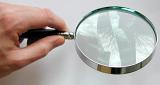 Man holding a round magnifying glass with a reflection on the lens over a blank sheet of white paper, high angle view