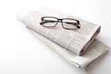 Pair of generic reading glasses on two folded newspapers over a white background with copy space arranged diagonally