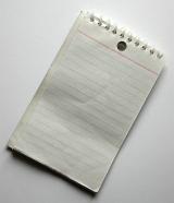 Blank spiral bound notepad with ruled lines lying diagonally on a white background