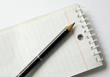 Pencil lying on a blank ruled spiral bound notepad viewed diagonally from above in a business or school concept