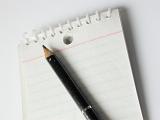 Close up view of short black pencil placed on a blank lined notepad against a white background
