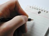 Man writing on a spiral bound notepad holding the pencil poised above the blank white ruled page, close up on his fingers
