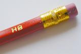 Back end of a red wooden graphite pencil with a small rubber held in place by a brass band and HB hardness marking stamped in gold