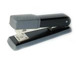 Grey and black office stapler for stapling paperwork with wire staples for filing and organization diagonally on white