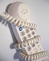 Generic white plastic telephone handset wrapped with coiled cord over neutral background