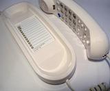 Land line telephone instrument with the receiver off the hook lying alongside it on a white surface, close up view