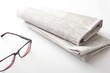 Folded newspaper with reading glasses on a white background with copy space conceptual of relaxation