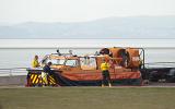 Men working on a coastguard hovercraft which is standing onshore above a sandy shallow bay