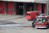 A fireman performs maintenance on a fire engine parked on the tarmac in a fire station courtyard