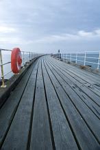 Safety lifering flotation device mounted on the metal railing on a wooden pier stretching out into the ocean