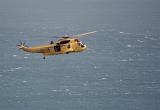 Search and rescue helicopter flying over the sea with the rear door open for quick access and to allow crew to assess any situation below