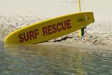 A surf rescue surfboard resting in a special bracket alongside the waters edge on the seashore ready for immediate use