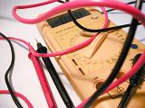 Close Up of Yellow Multimeter with Jumbled Red and Black Test Lead Cords on White Background