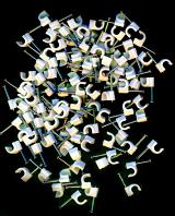 Random scatter of white plastic cable clips for attaching domestic cables and wires to a wall lying on a black background, over head view