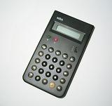 Black plastic desk calculator with round buttons and turned off electronic display, close-up on gray