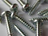 Close Up of Silver Colored Metal Screws with Phillips Drive Heads Scattered on White Background