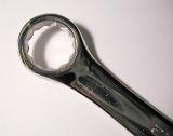 Ring end of a wrench tool or spanner, used in mechanics to turn rotary fasteners, high-angle close-up with copy space and shadow on gray