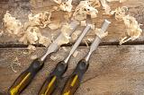 Three sharp woodworking chisels lying on rustic planks with fresh wood shavings conceptual of carpentry and construction