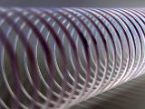Extreme close up of coiled metal spring with purple tones against a light background