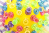 Macro view on various colored translucent plastic push pins stuck in yellow tennis ball