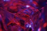 Selective focus view on glass cube with fractured corner surrounded by purple and blue