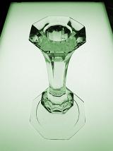Single elegant clear glass candlestick with a flared rim viewed high angle over a light background