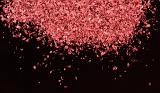 Pile of little pink glitter or paper scraps at top of frame over black background with copy space