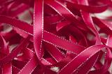 Close up of unraveled pink ribbon with silver trim against white background