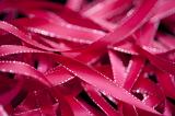 Close up of unwound deep pink satin ribbon with silver trim against a black background