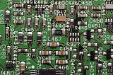 Close up of electrical components on green circuit board labeled with numbers and letters