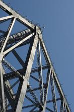 Massive steel bridge frame viewed from low angle against clear blue sky