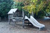 Kids playground with slide and climbing net under leafy green trees in autumn
