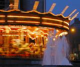 Motion blur on a brightly lit festive spinning merry-go-round at night with foreground fountain
