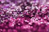 Close-up image of pile of pink and purple shiny glitter or sequins with tilt shift selective focus blur effect. Full frame background concept