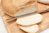 Round loaf of fresh white bread with a knife and two cut slices on a wooden bread board