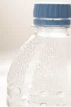Plastic bottle of cold water with beaded condensation and effervescence closed with a blue cap, close up detail of the shoulder and neck of the bottle