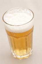Pint of refreshing golden lager with a frothy head in a tall glass, high angle view on grey
