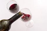 Pouring red wine into wine glasses from a bottle, close up high angle view over a white background with copyspace