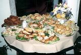 Buffet table at a catered event laden with platters of assorted savoury appetizers and snacks with a decorative vase of flowers behind