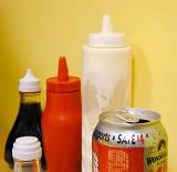 Plastic container with takeaway condiments including vinegar, mayonnaise and salt with a soda can in a chip shop