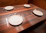 Wooden dinner table set with four place settings with cutlery and empty white ceramic plates