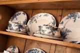 Blue and white dinner service displayed on the shelves of a rustic wooden dresser with plates and sauce boats