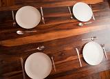 View from above of four empty place settings with cutlery and simple white plates on a dining table with decorative wood grain