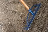 Raking new garden soil in spring with a metal toothed rake to level and sift soil for planting seeds or transplanting seedlings