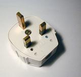 Three prong earthed British electrical plug for household appliances and hardware viewed from a high angle on a grey background