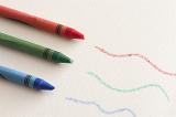 Green, red and blue colored wax crayons with squiggly hand drawn lines over textured paper viewed high angle