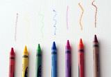 Row of colored wax crayons with wavy squiggles drawn above in the colors of the rainbow, overhead on white