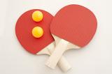 Two red wooden ping pong or table tennis bats with luminous yellow balls crossing over on a white background viewed from above