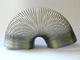 Retro metal slinky toy famous for its perpetual looping arched over on a white studio background