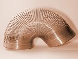 Old retro brown metallic slinky toy spring arched over on itself on an off white background